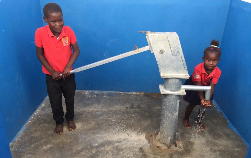 Haitian children pump drinking water from a hand pump that resulted from the Haiti Outreach project.