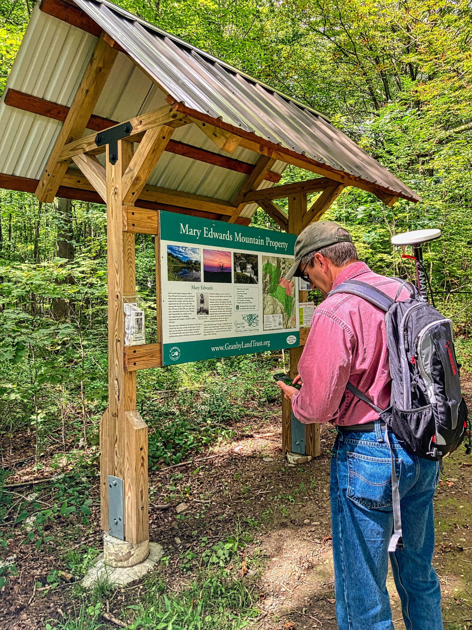 Steve Perry collects high accuracy GNSS GPS data in front of a trail, he is in the field for a land trust conservatorory using Esri ArcGIS Field Maps