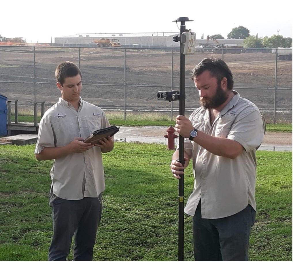 Two surveyors hold a rangepole with an Eos Arrow Gold GNSS receiver and a TruPulse 200X laser rangefinder from LTI. They are using the Eos Laser Mapping Solution to map hard-to-reach objects.