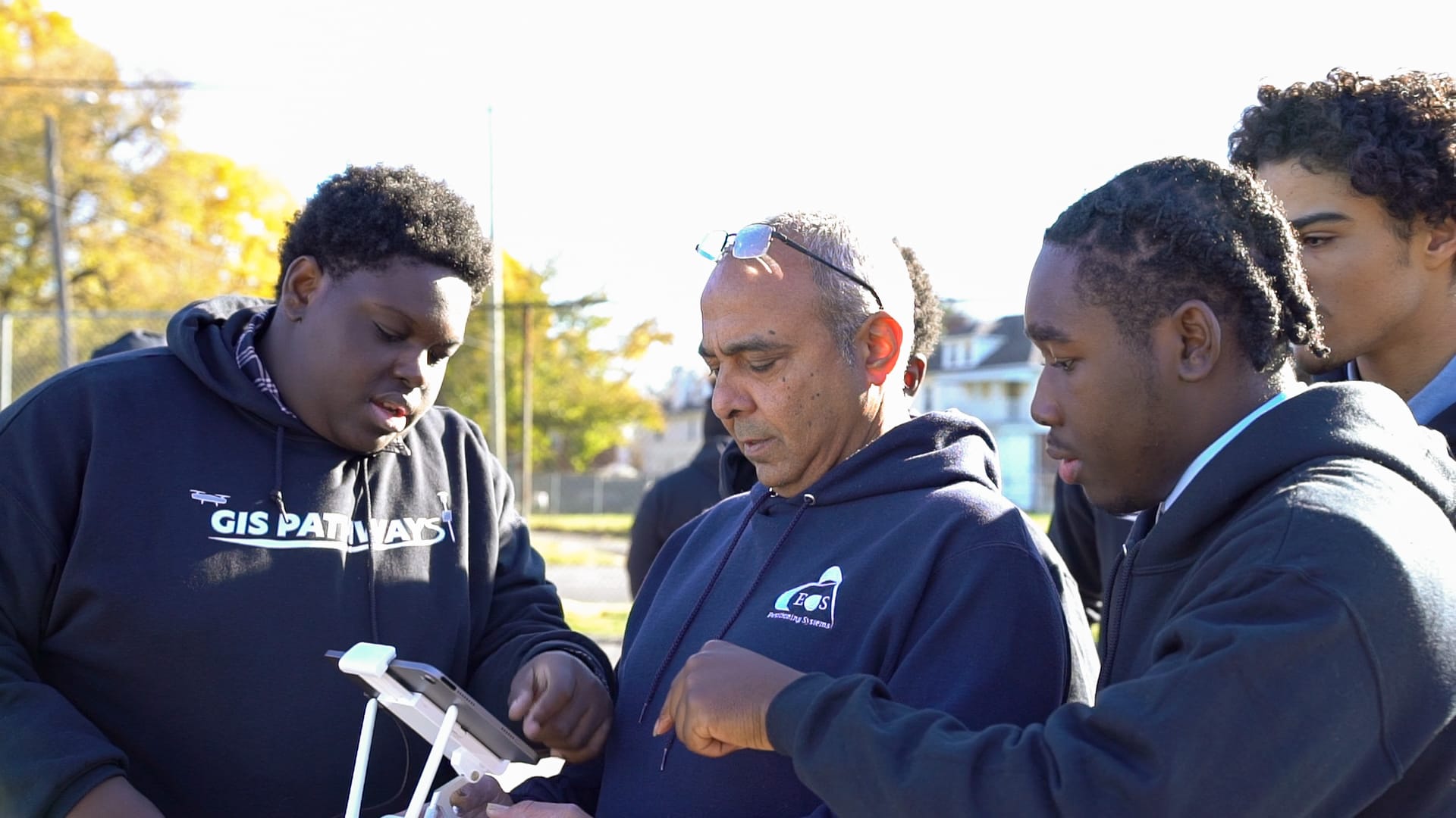 FDA Student Ambassadors Ashton (far left) and DeAnthony (far right) teach Eos Positioning Systems CTO Jean-Yves Lauture how to fly a drone outside Frederick Douglass Academy in Detroit.