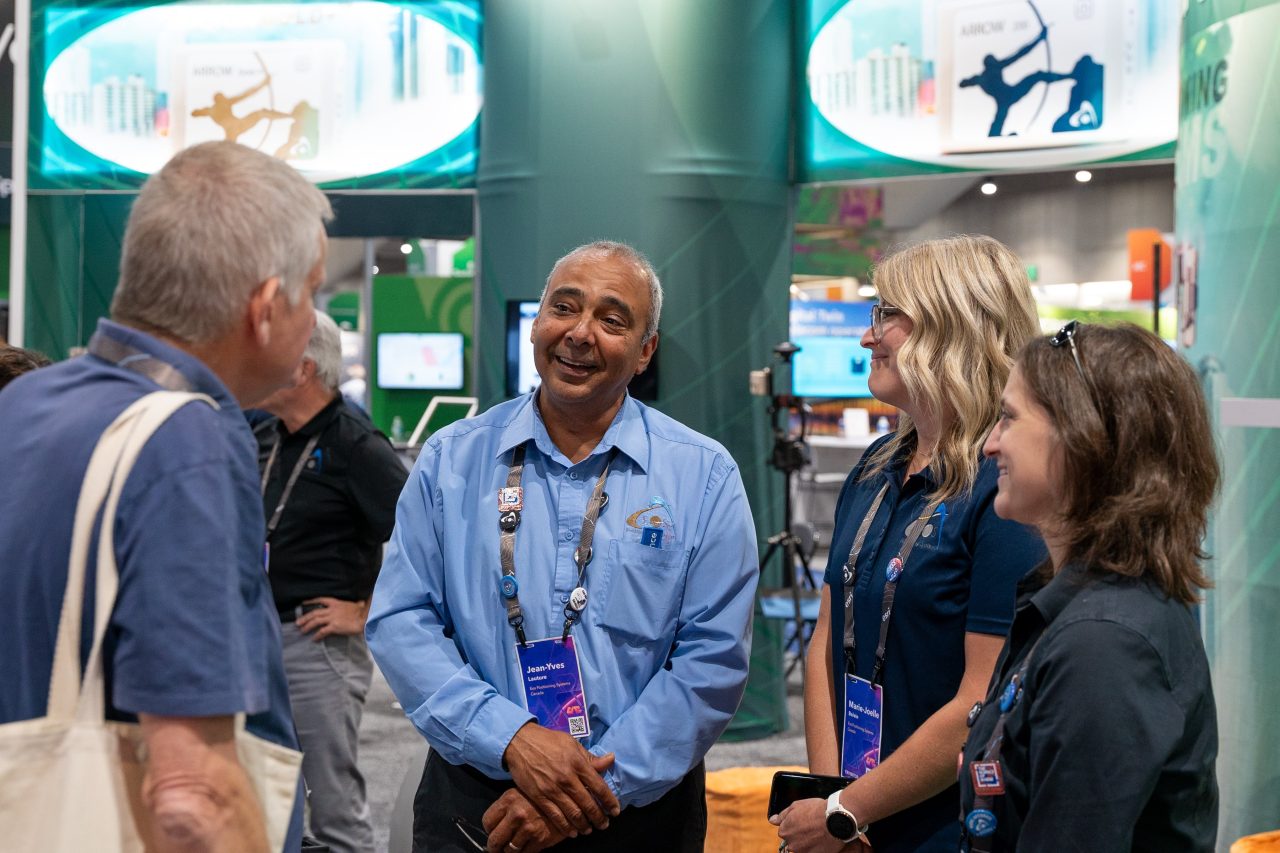 Eos CTO Jean-Yves Lauture and Eos employees Marie-Joëlle Boivin speak to a booth attendee at the 2023 Esri UC