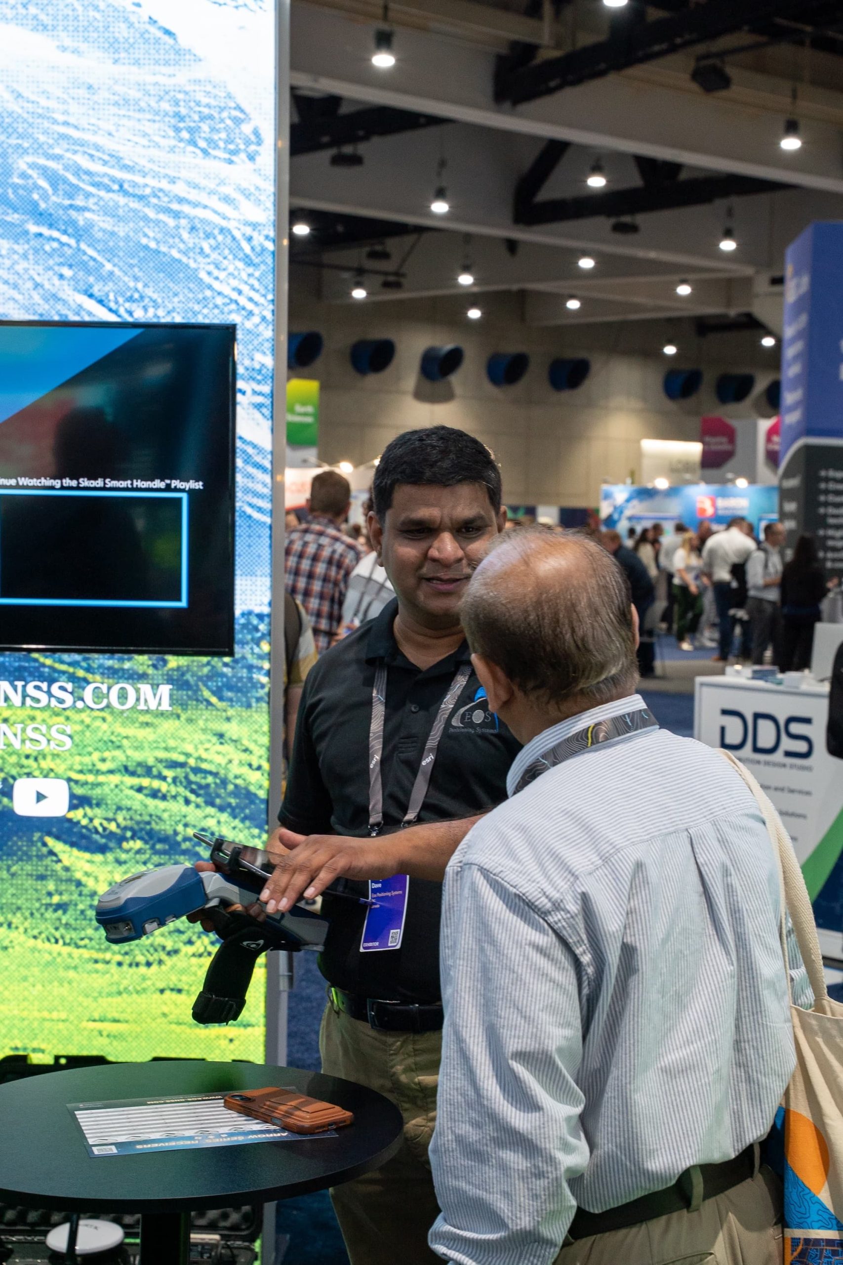 11 - Satyam Dave Speaks to a Customer at the Eos Booth copy Eos Regional Sales Manager Satyam Dave showed a customer how the new Eos phone and tablet brackets for Skadi GNSS receivers can hold any full-size tablet or phone.